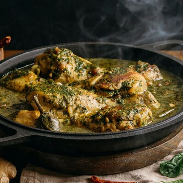 Steaming Indian chicken curry with green herbs in a black cast iron pan, with ginger and chilies.