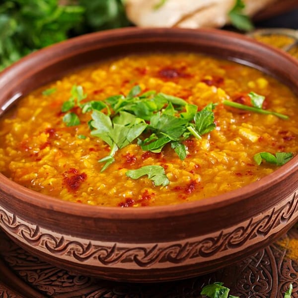 A rustic bowl of Dosa Kitchen's yellow lentil dal, garnished with fresh cilantro and red spice.