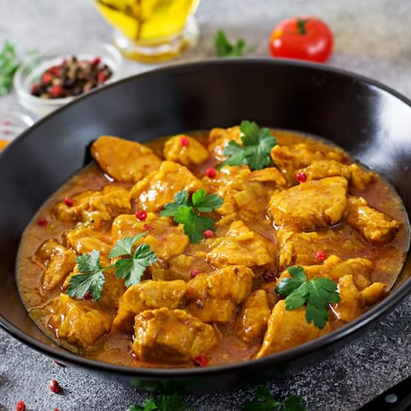 Dosa Kitchen's chicken curry, garnished with fresh parsley and red peppercorns, in a black bowl.