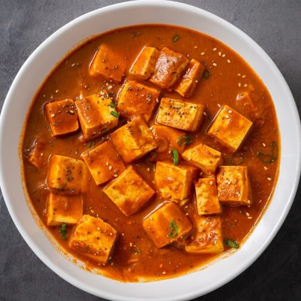 Dosa Kitchen's paneer butter masala, featuring paneer cubes in a rich, orange-red sauce, garnished with seeds.